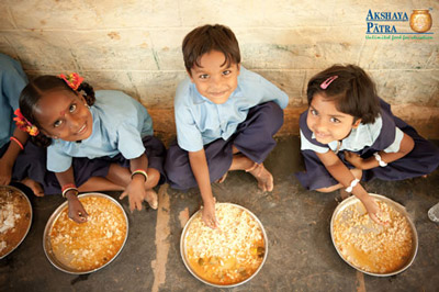 Children smiling sat on the floor with bowls of food 